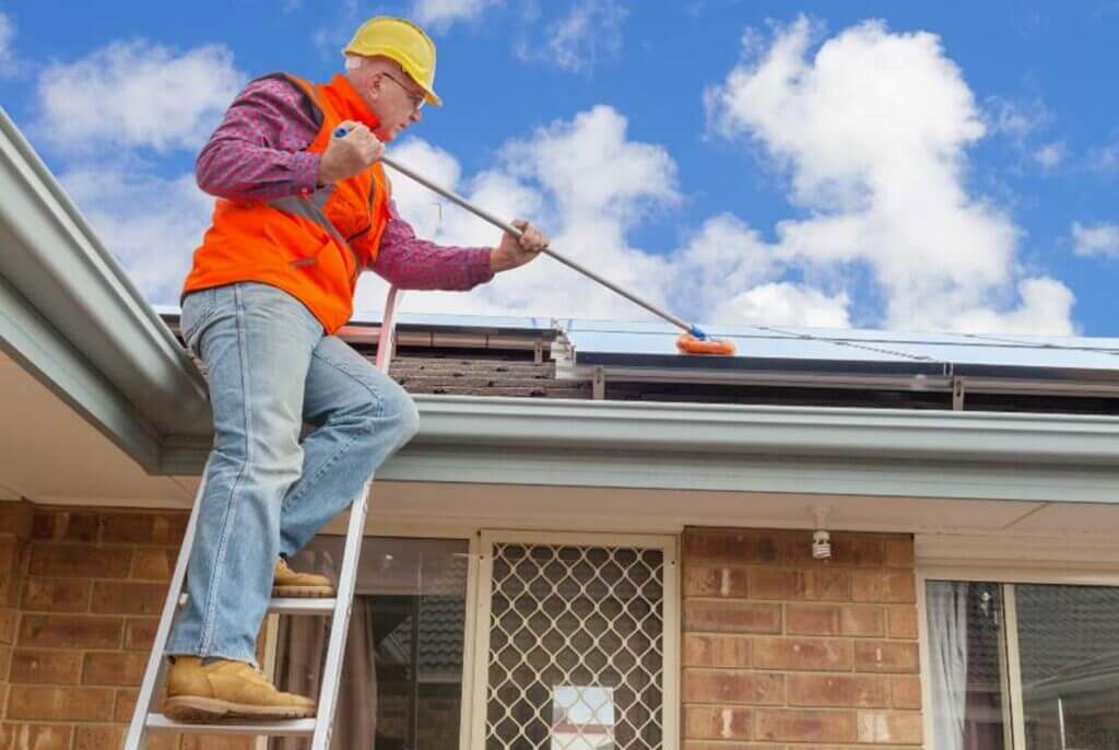 A man on a ladder cleaning the roof of a house in South Florida.